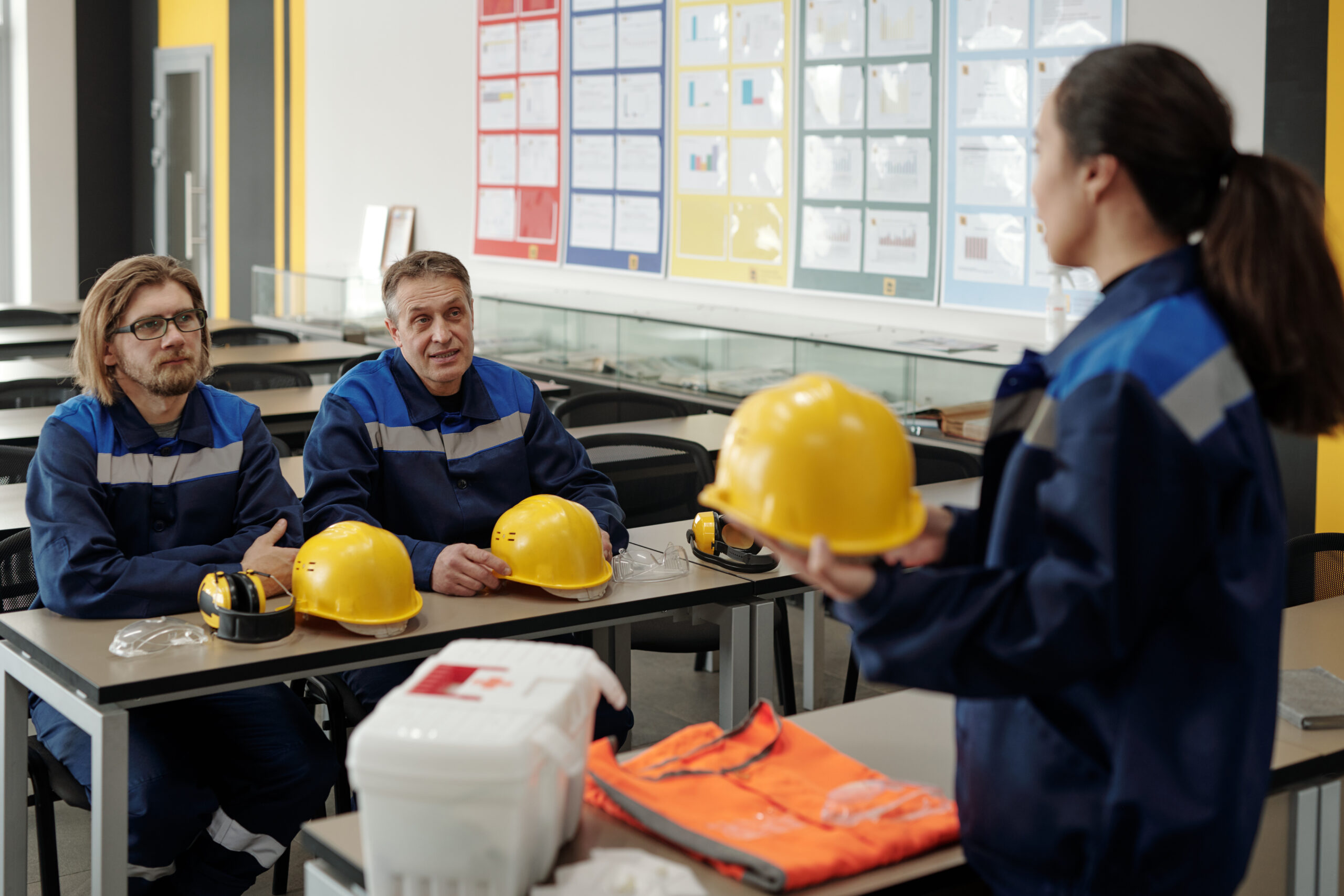 Instructor explaining occupational safety rules Female instructor holding hardhat and explaining occupational safety rules to workers sitting at table