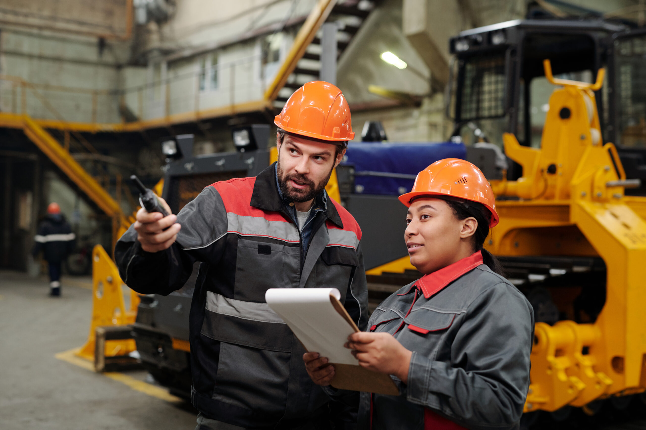 Two interracial workers of industrial plant discussing new equipment Two interracial workers of industrial plant discussing new equipment for machinery production while foreman pointing forwards